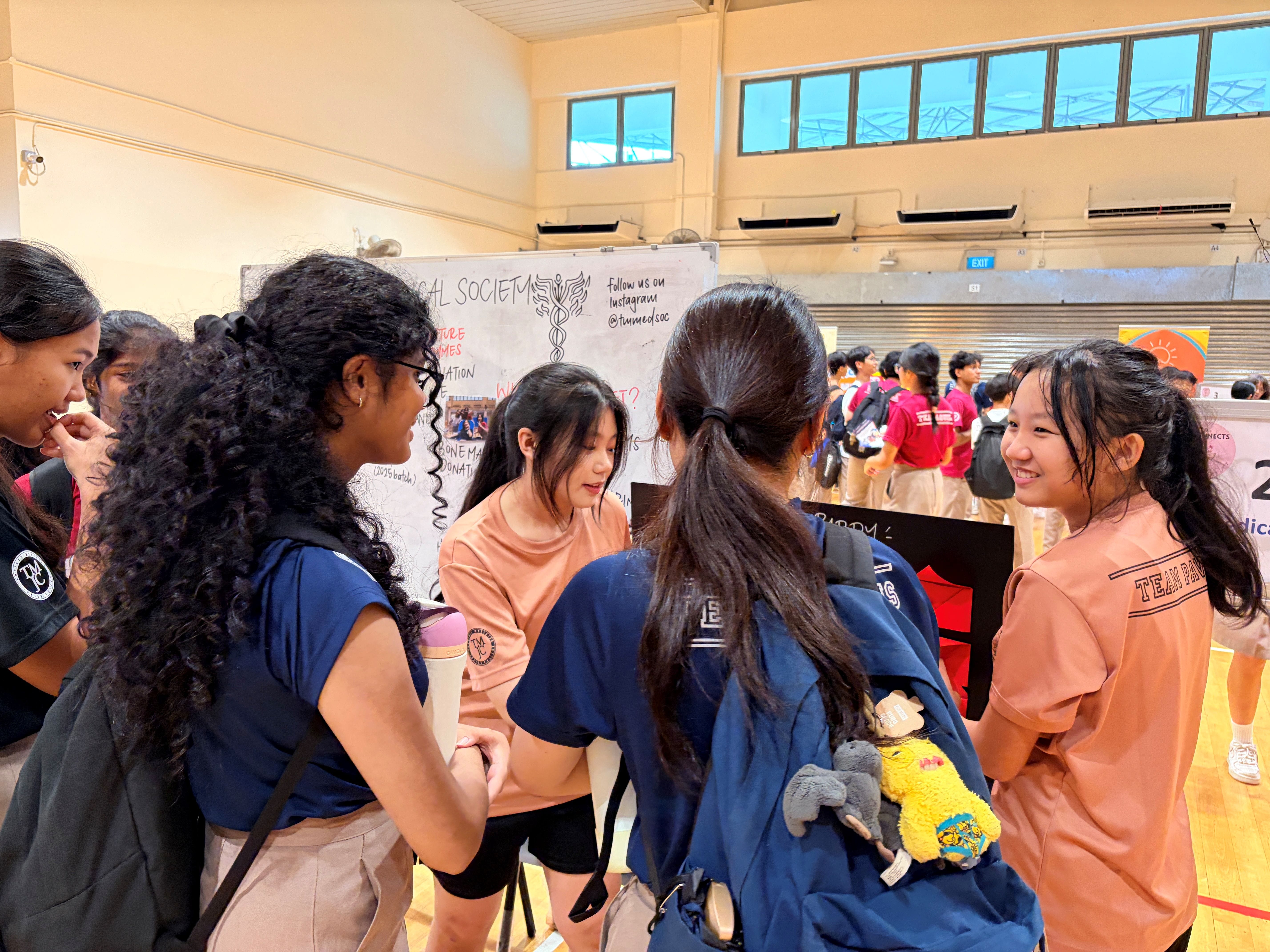 A group of students gathered around a Medical Society booth, listening to a student representative explain the club's activities.